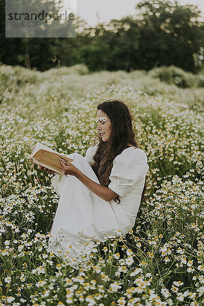 Frau liest Buch  während sie auf einem Blumenfeld sitzt