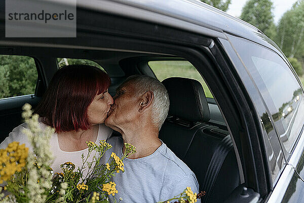 Liebevolles Paar küsst sich  während es mit einem Blumenstrauß im Auto sitzt