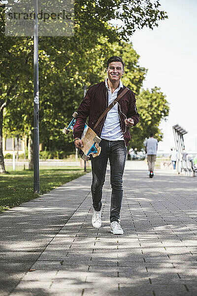 Mann mit Skateboard geht auf Fußweg