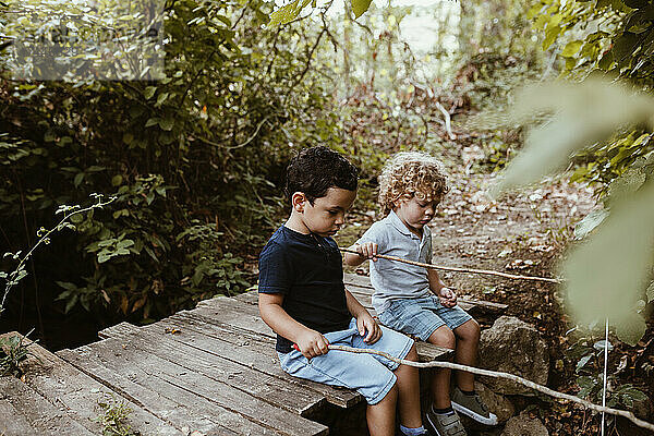 Junge und männlicher Freund sitzen auf Steg beim Angeln im Wald