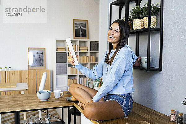 Glückliche junge Frau hält digitales Tablet auf der Küchentheke