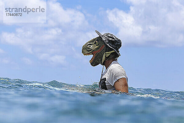 Mann mit Dinosauriermaske im Meer an sonnigen Tagen