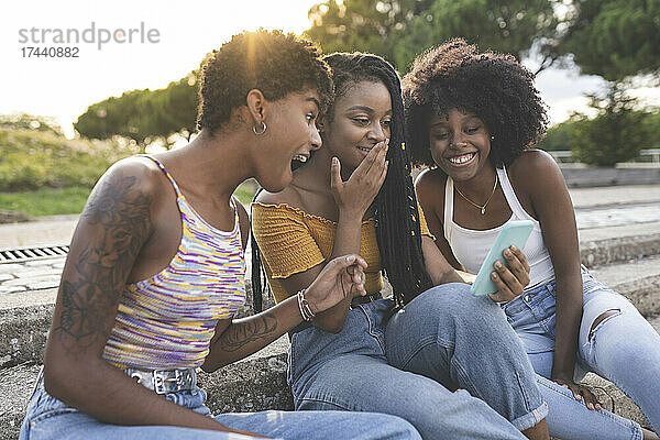 Überraschte Freundinnen schauen im Park auf ihr Mobiltelefon