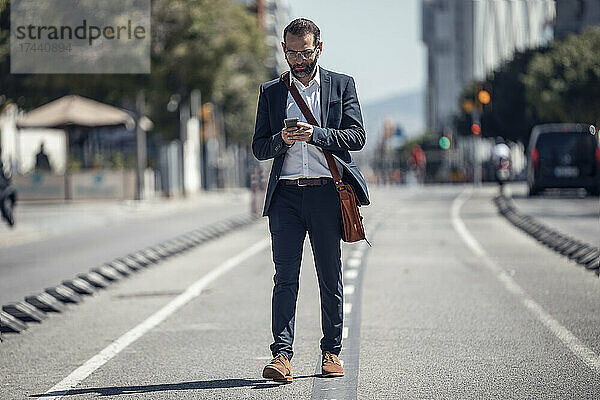 Männlicher Geschäftsprofi nutzt Mobiltelefon beim Spaziergang in der Stadt