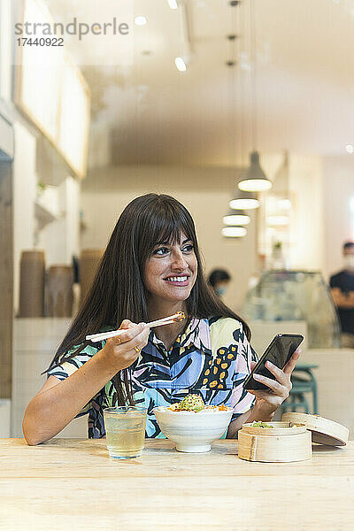 Glückliche Frau mit Handy beim Essen im Restaurant