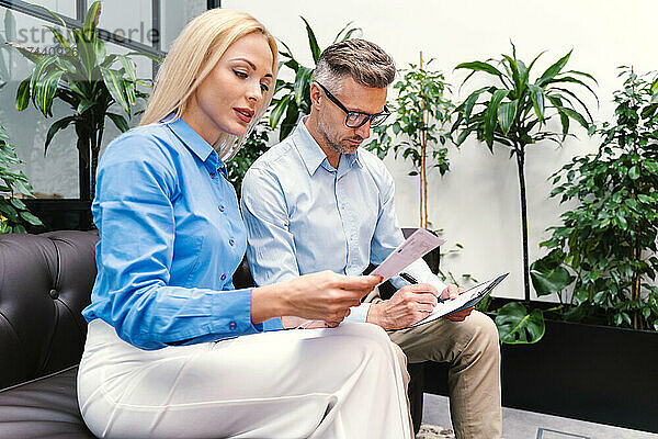 Eine Frau liest beruflich ein Dokument  während sie neben einem männlichen Kollegen im Büro sitzt