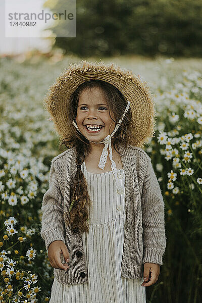 Glückliches Mädchen mit Hut  das auf dem Blumenfeld steht