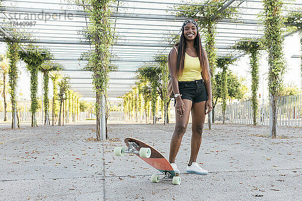 Lächelnde Frau steht mit Skateboard auf Fußweg