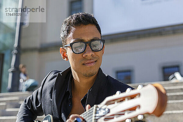 Hübscher männlicher Gitarrist mit Brille  der an sonnigen Tagen Gitarre spielt