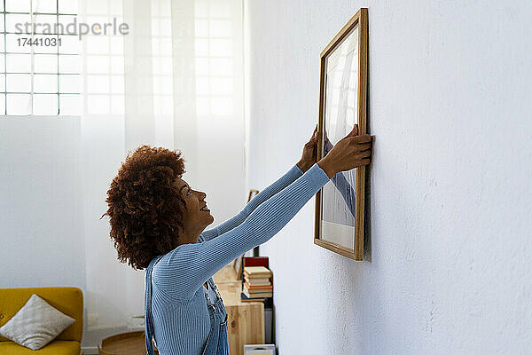 Rothaarige Frau installiert Fotorahmen an weißer Wand