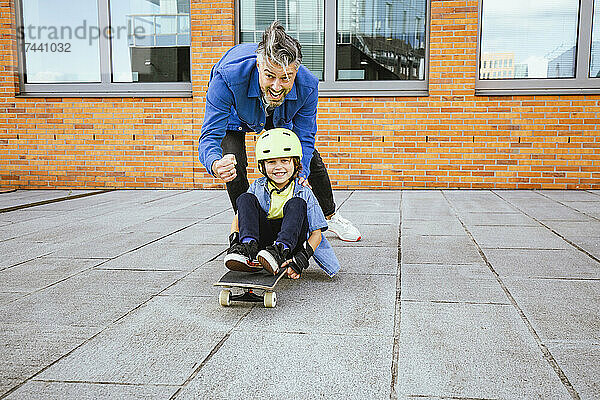 Verspielter Vater und Sohn spielen mit Skateboard auf Fußweg