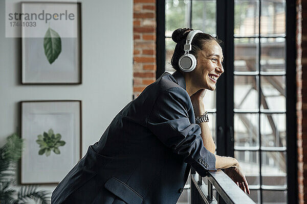 Glückliche Geschäftsfrau  die im Büro Musik über drahtlose Kopfhörer hört