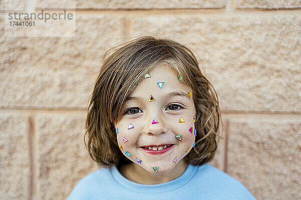Niedliches lächelndes Mädchen mit Konfetti im Gesicht vor der Wand