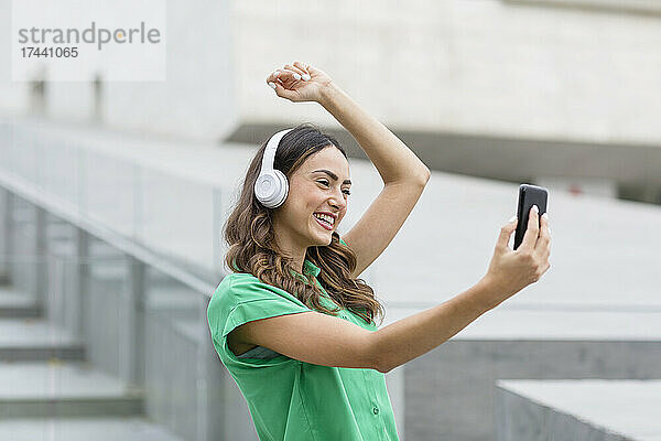 Glückliche Frau mit kabellosen Kopfhörern  die ein Selfie über ihr Smartphone macht