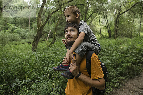 Mann mit Rucksack trägt Jungen auf Schultern im Wald