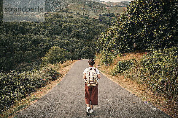 Touristin mit Rucksack und Blick auf den Berg beim Gehen auf der Straße