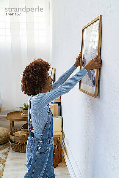 Afro-Frau hängt Bilderrahmen an Wohnzimmerwand