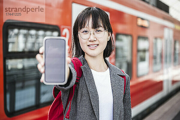 Teenager-Mädchen zeigt Smartphone am Bahnhof