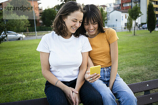 Glückliches lesbisches Paar benutzt Smartphone auf Bank