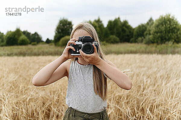 Blondes Mädchen fotografiert mit der Kamera auf einem Weizenfeld
