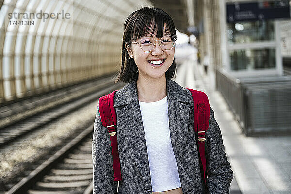 Lächelndes Teenager-Mädchen mit Rucksack am Bahnhof