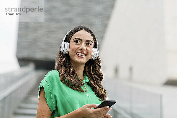 Lächelnde Frau mit kabellosen Kopfhörern und Mobiltelefon
