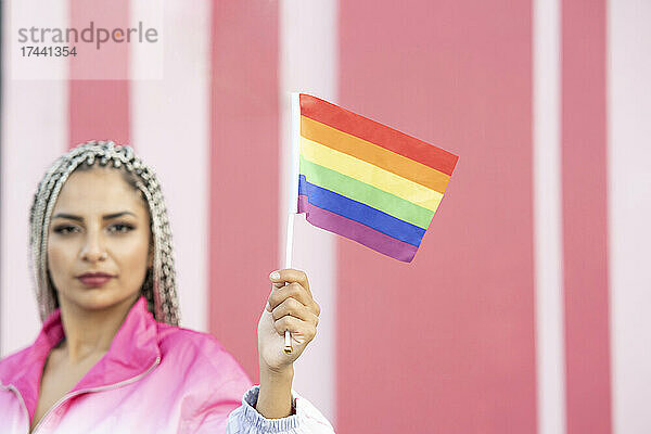 Frau hält Regenbogenfahne vor rosa Wand