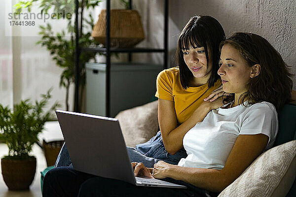 Lesbisches Paar benutzt Laptop  während es zu Hause auf dem Sofa sitzt