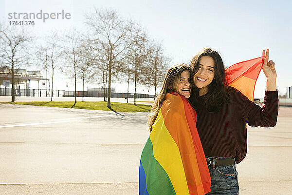 Junges lesbisches Paar mit Regenbogenfahne an sonnigen Tagen