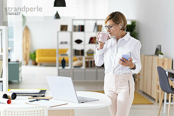 Geschäftsfrau mit Mobiltelefon trinkt Kaffee im Büro