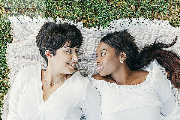 Lächelnde Frauen schauen einander an  während sie auf einer Decke liegen