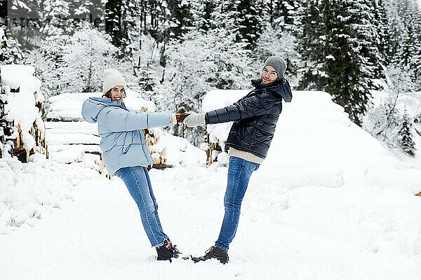 Verspieltes junges Paar hält Händchen im Schnee