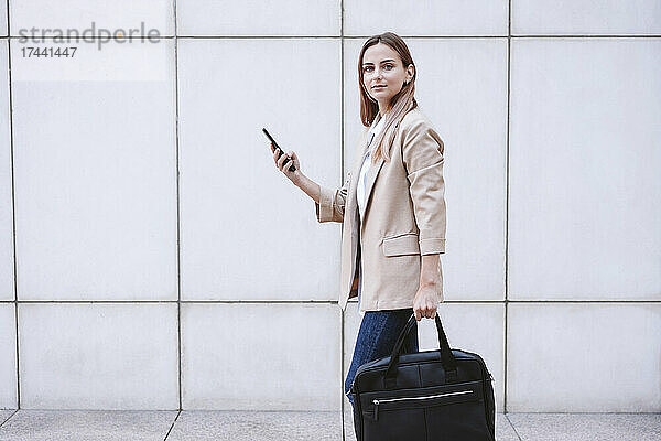 Junge Geschäftsfrau mit Aktentasche und Smartphone geht auf Fußweg