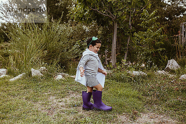 Fröhlicher Junge mit lila Stiefeln läuft auf der Wiese