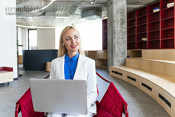 Nachdenkliche Geschäftsfrau mit Laptop schaut weg  während sie im Büro sitzt