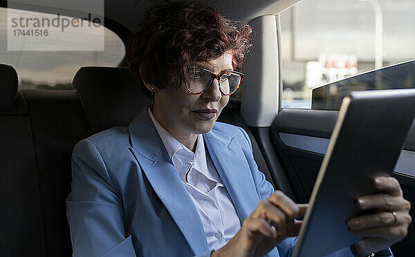 Reife Geschäftsfrau nutzt digitales Tablet  während sie im Auto sitzt