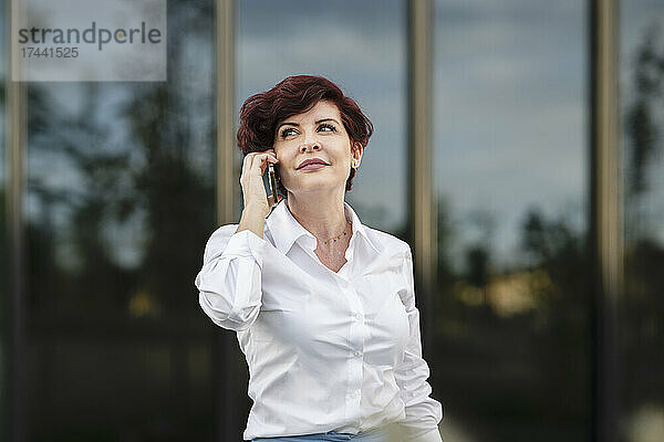 Schöne berufstätige Frau  die vor dem Bürogebäude mit dem Mobiltelefon spricht