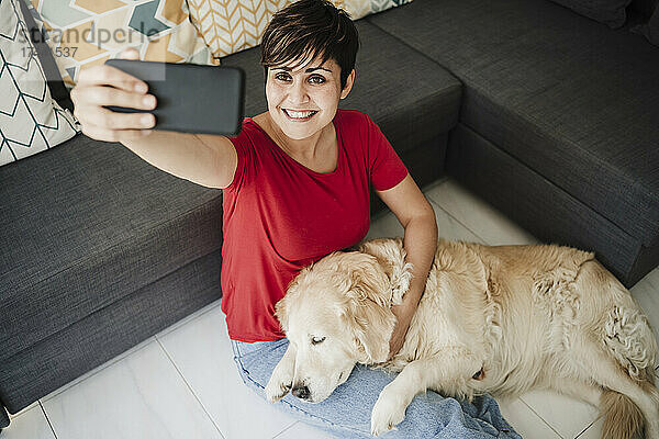 Frau macht Selfie mit Hund  während sie zu Hause im Wohnzimmer sitzt