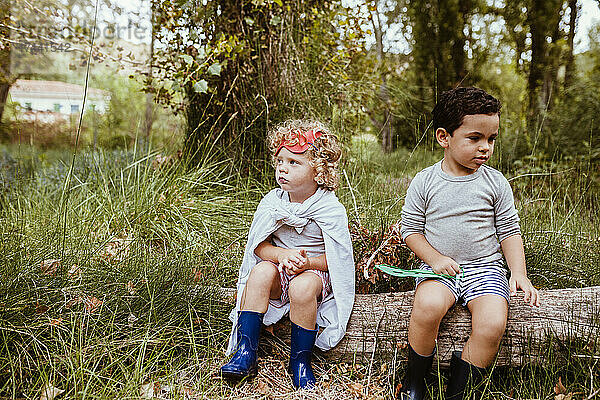 Süße Jungs in Stiefeln sitzen auf einem Baumstamm im Wald