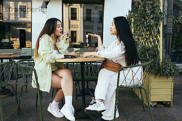 Junge Frauen reden  während sie im Straßencafé sitzen