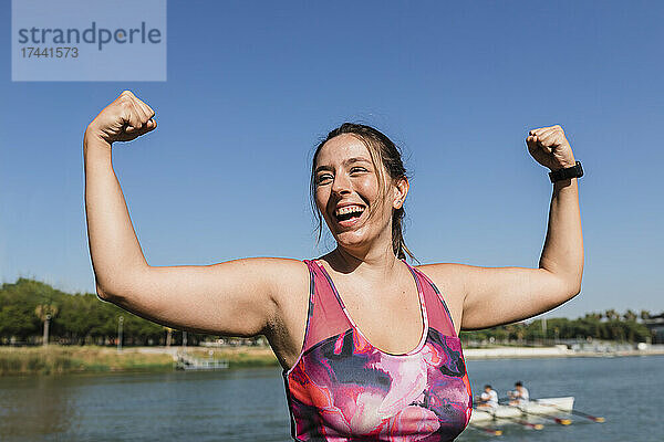 Sportlerin lacht  während sie am Flussufer ihre Muskeln spielen lässt
