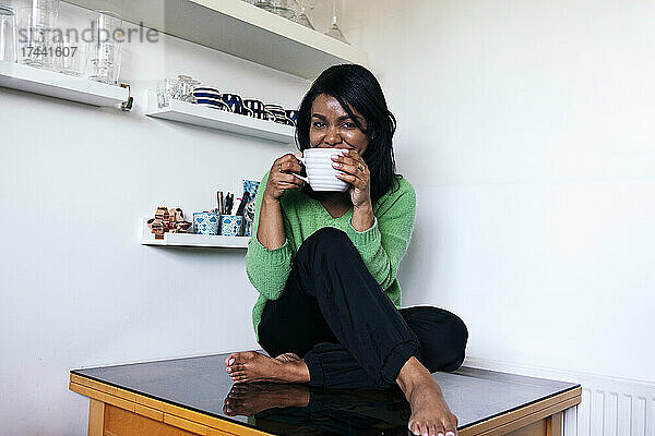 Frau trinkt Kaffee  während sie am Tisch in der Küche sitzt