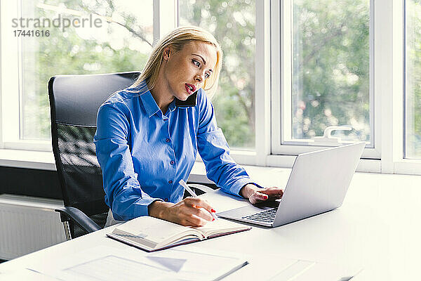 Weibliche Geschäftsfrau  die während der Arbeit im Büro auf dem Smartphone spricht
