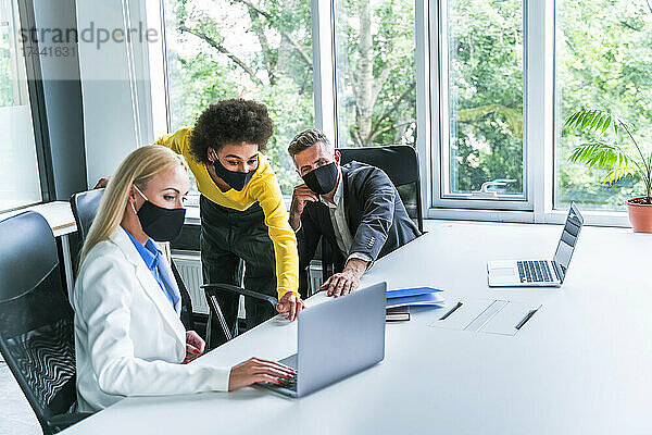 Männliche und weibliche Geschäftsleute tragen bei der Arbeit im Büro eine schützende Gesichtsmaske