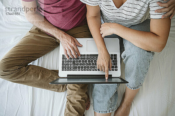Frau berührt Bildschirm  während Mann mit Laptop im Bett sitzt