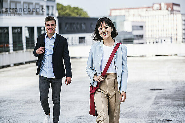 Lächelnde Geschäftsfrau geht mit männlichem Kollegen auf dem Dach spazieren