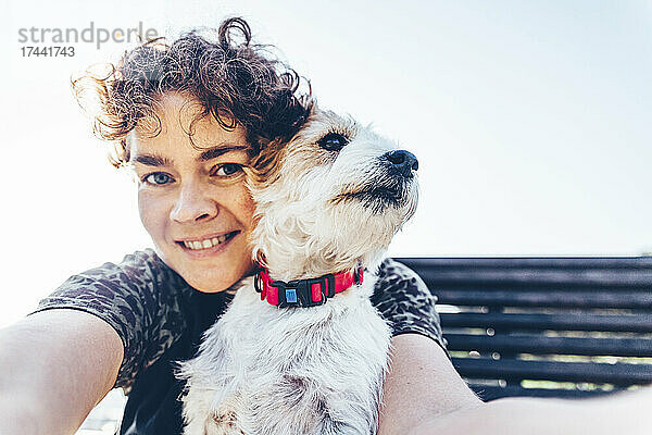 Lächelnde Frau mit Jack Russell Terrier  die an einem sonnigen Tag ein Selfie macht
