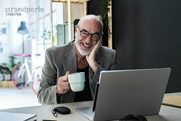 Glücklicher älterer Geschäftsmann mit Kaffeetasse am Arbeitsplatz