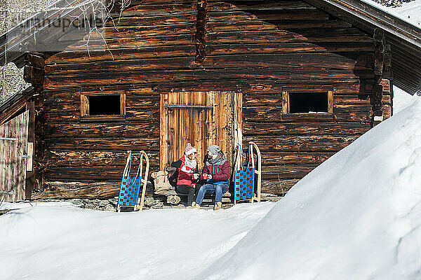 Paar genießt Getränk  während es im Winter in der Nähe der Hütte sitzt