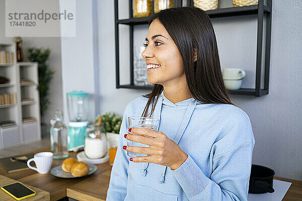 Lächelnde junge Frau hält zu Hause ein Glas Wasser